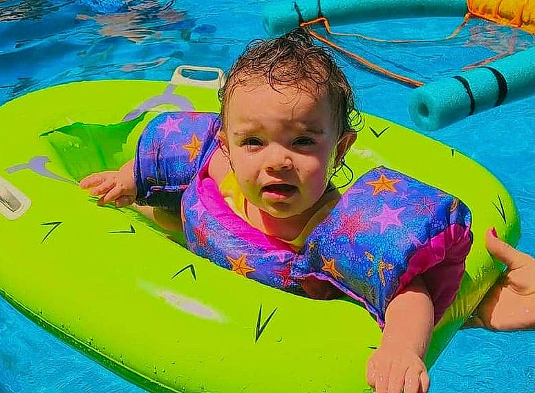 Ariana is registered to the contest to win money with this photo: aqua, azure, baby, baby_float, child, comfort, facial_expression, fun, games, green, happy, inflatable, leisure, outdoor_recreation, person, personal_protective_equipment, product, recreation, summer, toddler