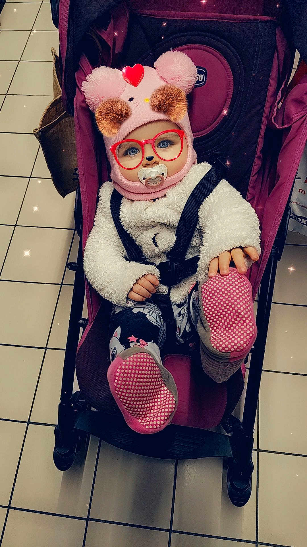 Kimberley a rejoint le concours — aidez-le/la à gagner de superbes lots ! baby, stroller, pacifier, hat, pom_poms, glasses_filter, heart_filter, coat, toddler, child, floor_tiles, shopping_bag, footwear, leggings, patterned_clothing, indoor, cute, smiling, seatbelt, playful_filter