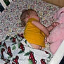 toddler, sleeping, crib, blanket, stuffed_animal, yellow_shirt, pink, toy, child, bedroom, floral_sheet, curly_hair, rest, cozy, indoor, baby, peaceful, nap, comfort, clothing