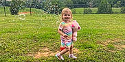 Jillian is registered to the contest to win money with this photo: bubbles, child, cloudy_sky, cute, daytime, fence, field, grass, greenery, nature, outdoor, person, playing, shoes, shorts, smiling, teddy_bear, toddler, toy, tshirt