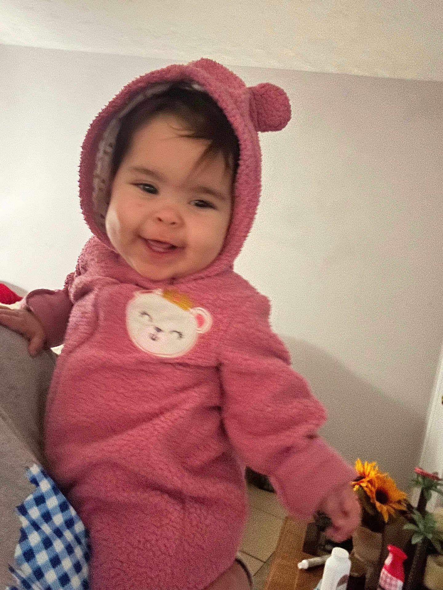 Ashley is registered to the contest to win money with this photo: baby, child, hoodie, pink_clothing, smiling, face, person, indoors, flower, sunflower, table, bottle, plant, hand, cute, cozy, warm_clothing, home, infant, portrait