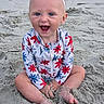 baby, child, beach, sand, smile, happy, headband, bow, swimsuit, floral_pattern, sitting, barefoot, outdoor, sunlight, cute, playful, portrait, person, infant, summer