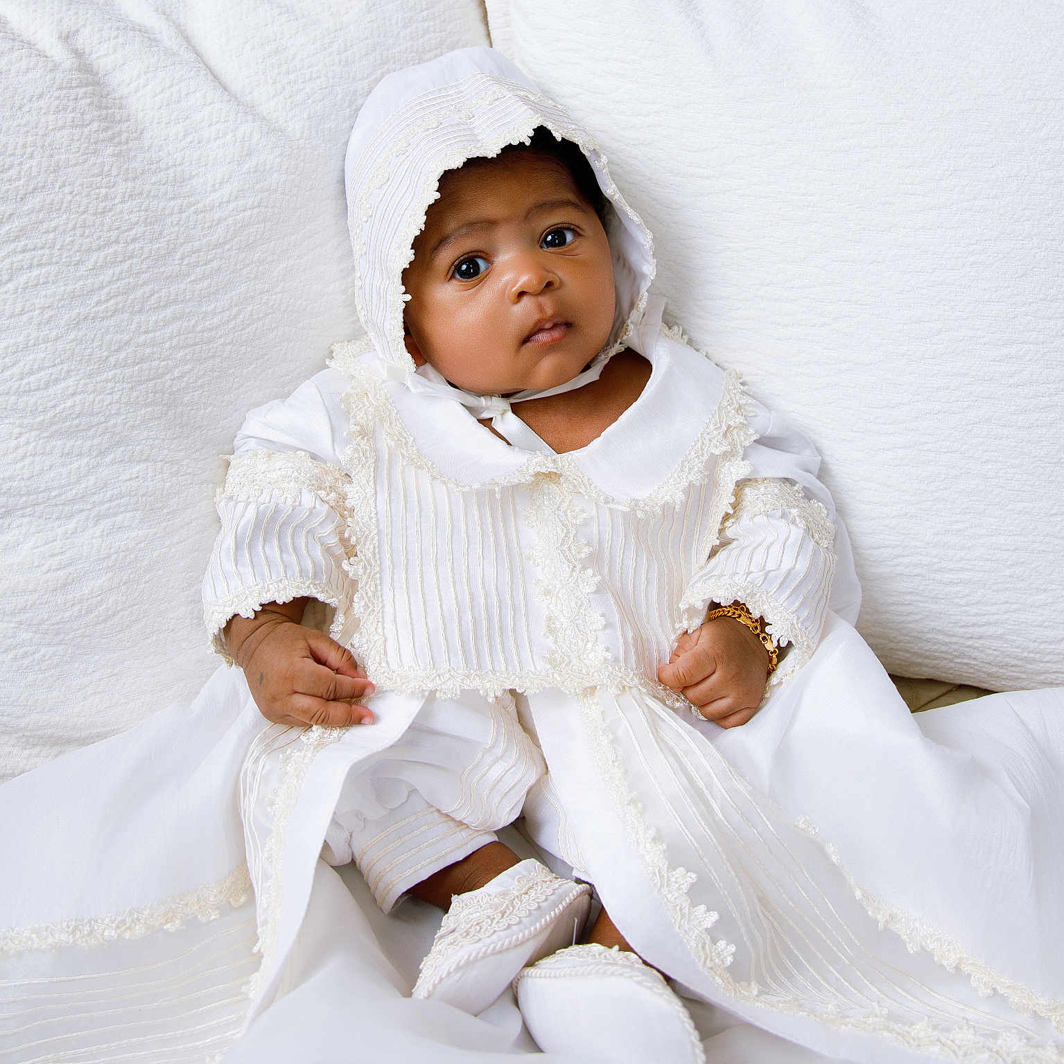Lior joined the competition — help win amazing prizes! baby, infant, child, white_clothing, bonnet, christening_gown, cushion, fabric, portrait, sitting, cute, indoors, soft_lighting, closeup, face, hands, footwear, bracelet, serene, curious
