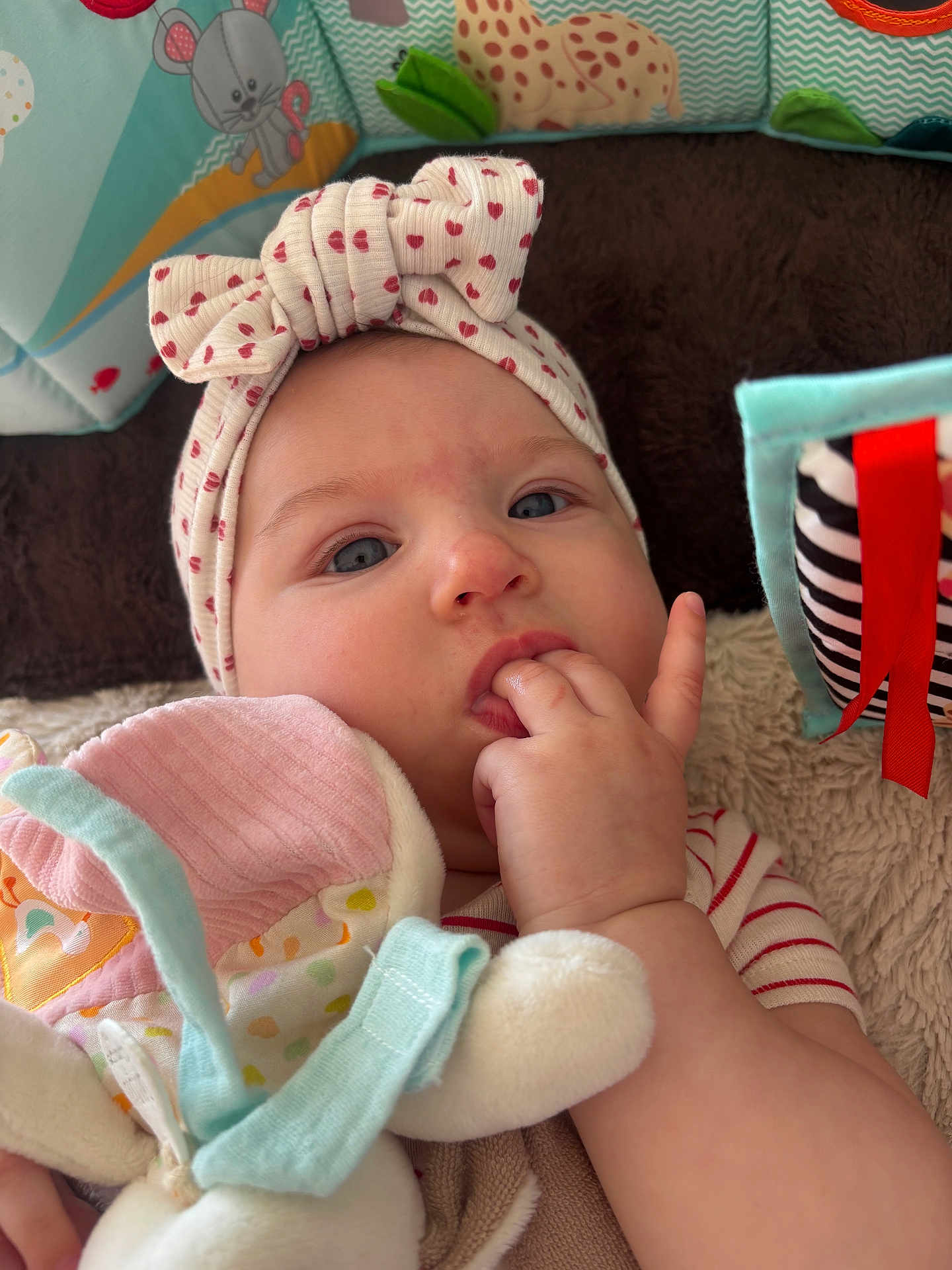 Romy participe au concours pour gagner de l'argent avec cette photo : baby, infant, face, headband, bow, blue_eyes, fingers_in_mouth, hand, toy, plush_toy, blanket, playmat, striped_clothing, closeup, portrait, soft_toy, nursery, cheek, skin, cute