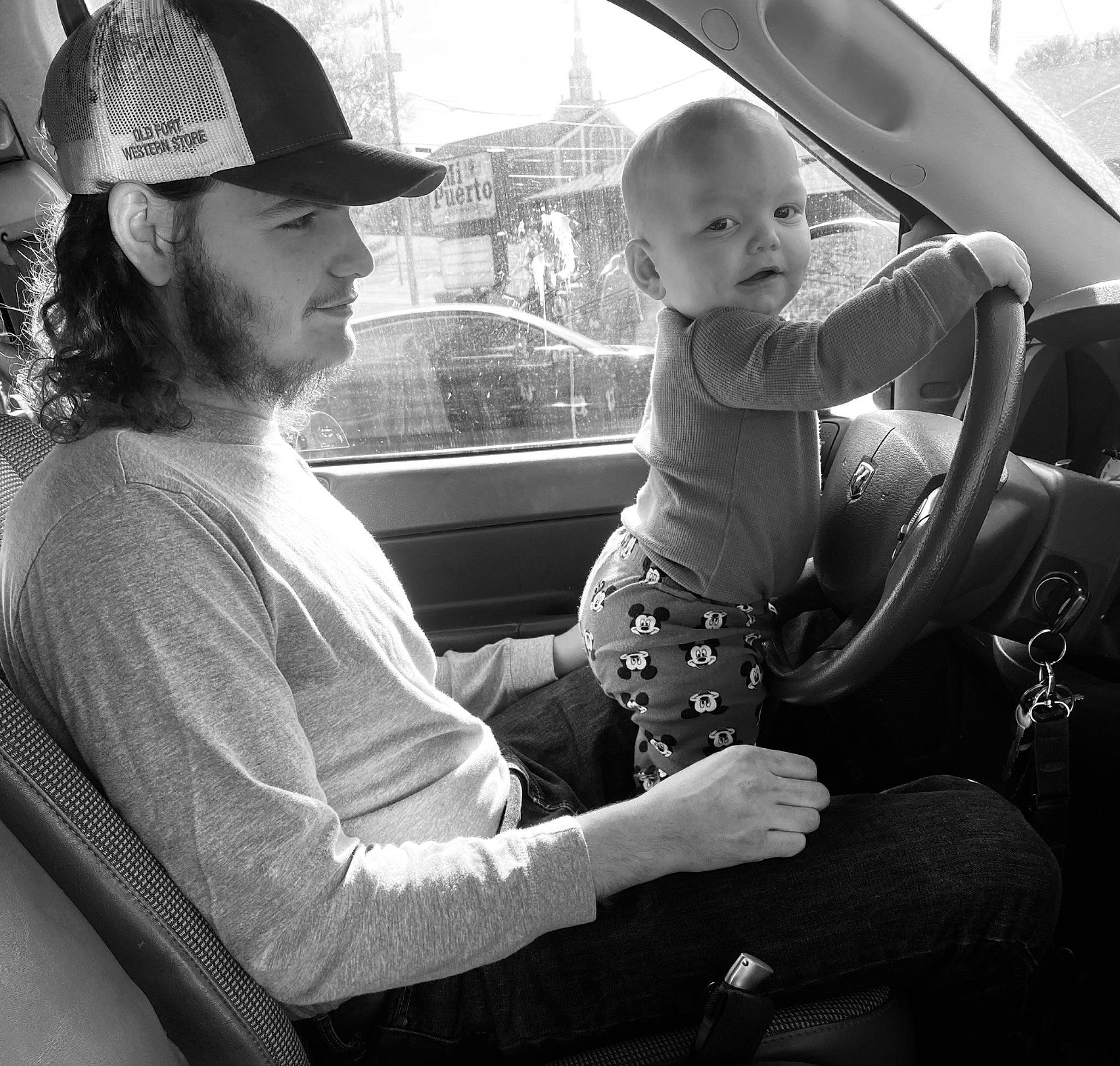 Oliver is registered to the contest to win money with this photo: automotive_design, automotive_exterior, black_and_white, car, car_seat, car_seat_cover, cool, fedora, hat, headwear, monochrome, monochrome_photography, motor_vehicle, person, standing, steering_wheel, style, sun_hat, toddler, vehicle