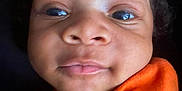 Amun-Ra is registered to the contest to win money with this photo: baby, child, close_up, curly_hair, cute, expression, eyes, face, head, indoors, infant, mouth, newborn, nose, orange_clothing, person, portrait, skin, soft_light, young