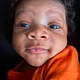 baby, infant, face, curly_hair, orange_clothing, close_up, child, skin, portrait, cute, expression, person, young, head, eyes, mouth, nose, soft_light, indoors, newborn