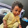toddler, child, yellow_onesie, curly_hair, indoor, bed, toy, baby_gear, winnie_the_pooh, playpen, person, cute, infant, face, hand, sitting, expression, curious, young_child, cozy
