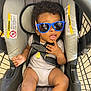 baby, sunglasses, stroller, child, curly_hair, infant, seatbelt, warning_label, hand, clothing, casual, shopping_cart, metal, cute, expression, young_child, indoor, person, seat, portrait