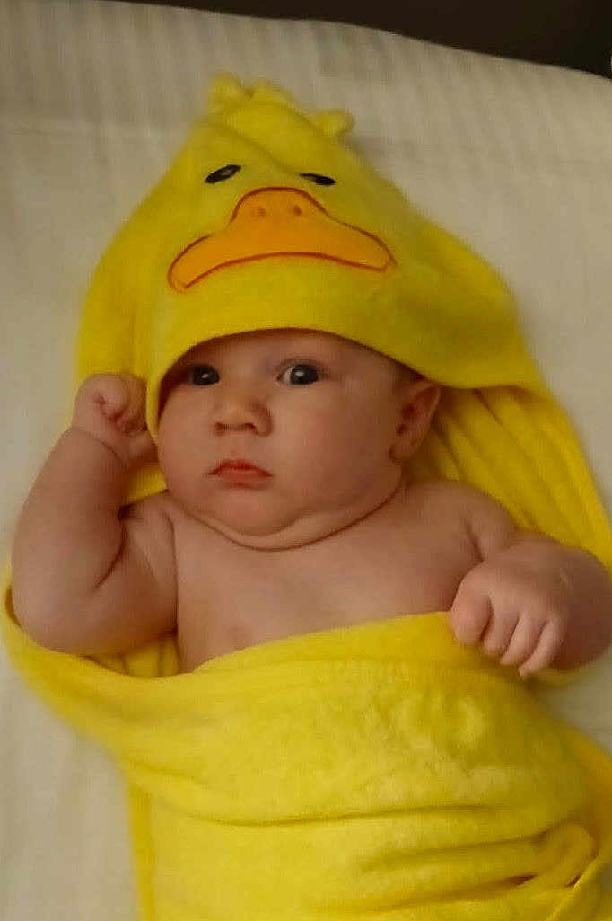 Aiden joined the competition — help win amazing prizes! baby, child, yellow_towel, duck_hood, cute, infant, wrapped, blanket, face, eyes, skin, hand, expression, indoors, bed, soft, adorable, portrait, newborn, curious