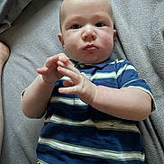 Aiden is registered to the contest to win money with this photo: baby, child, infant, striped_shirt, blue_shirt, green_stripes, polo_shirt, lying_down, blanket, gray_blanket, hands, face, expression, indoors, casual_clothing, young_child, portrait, skin, head, person