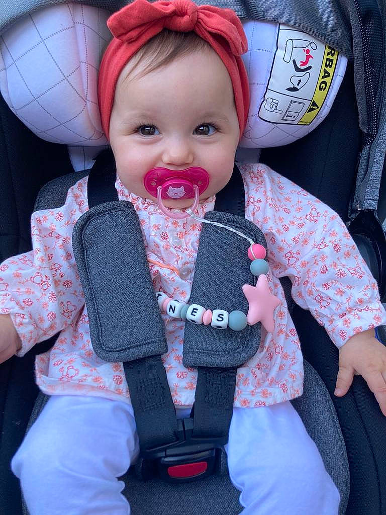 Inès participe au concours pour gagner de l'argent avec cette photo : baby, baby_carriage, baby_products, baby_toddler_clothing, cap, car_seat, cheek, child, doll, eye, head, human_body, outerwear, person, pink, seat_belt, skin, sleeve, smile, toddler