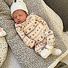newborn, baby, sleeping, onesie, hat, bear_pattern, blanket, soft_texture, cozy, infant, bed, cushion, white_socks, cute, resting, indoors, neutral_colors, peaceful, portrait, child