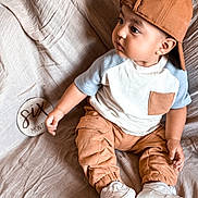 Juan is registered to the contest to win money with this photo: baby, child, infant, cap, brown_clothing, white_shoes, sitting, blanket, milestone_sign, six_months, curious, side_view, indoor, portrait, casual_clothes, cute, soft_lighting, cozy, young_child, fabric