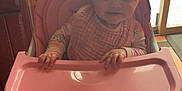 Astrid is registered to the contest to win money with this photo: baby, high_chair, pink, bib, pajamas, indoor, window, snow, hands, face, smile, person, child, furniture, floor, door, curtains, table, home, cozy