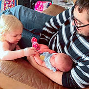 Astrid joined the competition — help win amazing prizes! baby, toddler, man, glasses, striped_shirt, couch, leather, socks, floor, shoes, rug, table, papers, cage, wood_floor, indoor, family, child, curious, holding