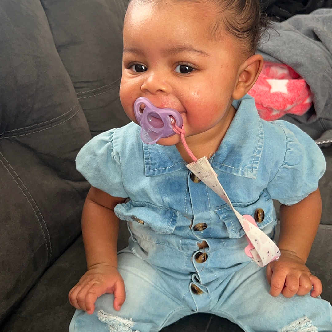 Nevaylah is registered to the contest to win money with this photo: baby, bodypart, clothing, couch, cushion, cutlery, face, finger, footwear, furniture, head, homedecor, jeans, pants, person, photography, portrait, shoe, sitting, spoon