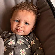 Isabel joined the competition — help win amazing prizes! baby, child, curly_hair, onesie, floral_pattern, drool, cushioned_seat, indoor, cute, portrait, infant, relaxed, hand, face, blue_eyes, clothing, comfort, young, person, seat