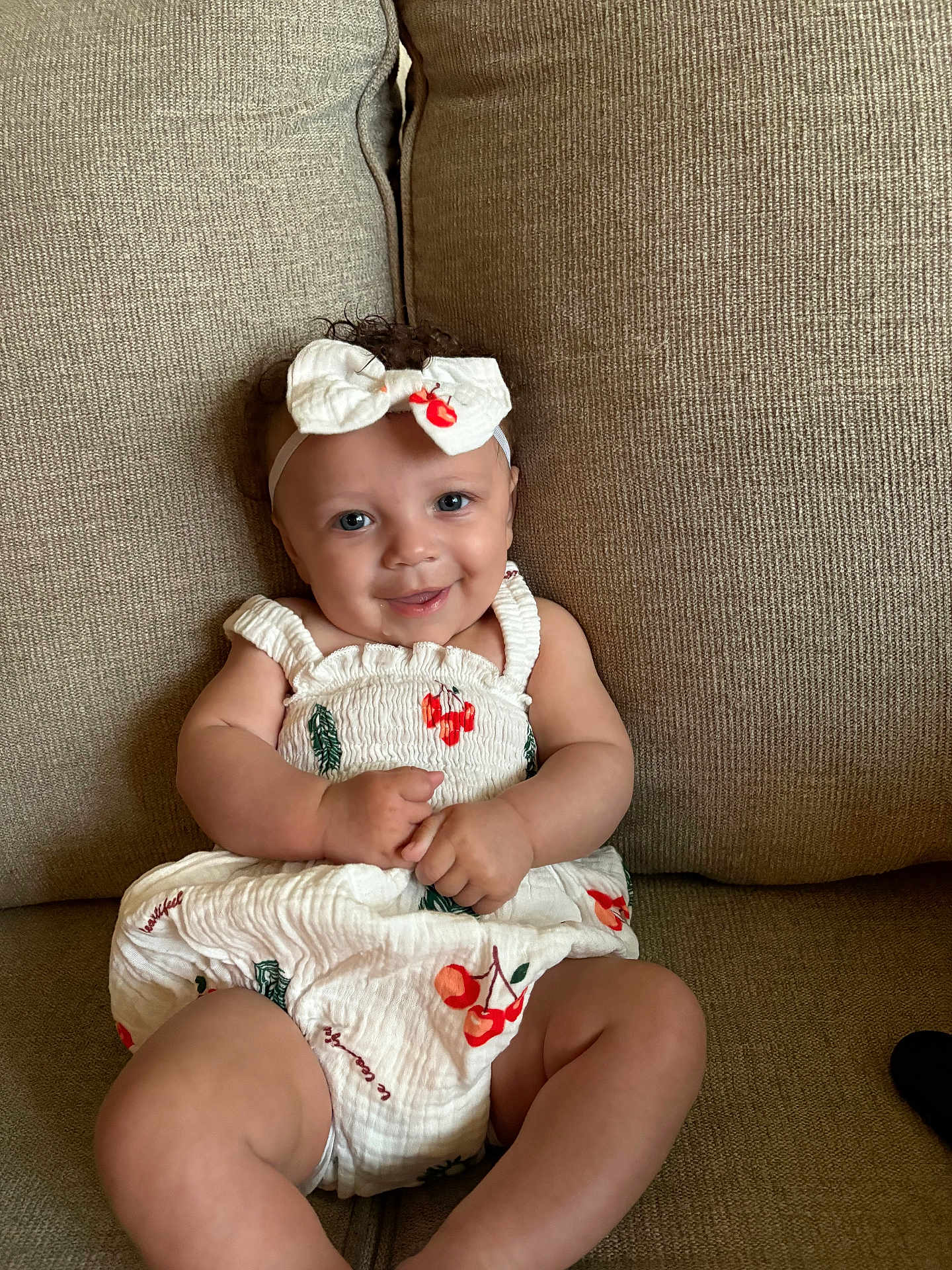 Isabel joined the competition — help win amazing prizes! baby, child, smiling, sitting, dress, headband, bow, cherry_pattern, couch, furniture, happy, cute, infant, portrait, indoor, skin, face, person, clothing, young