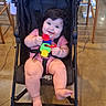 baby, child, stroller, smiling, happy, portrait, toy, colorful_toy, pink_clothing, seated, infant, face, eyes, hair, indoor, restaurant, chair, floor, wheels, family_outing