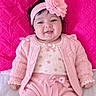 baby, infant, child, portrait, smiling, sitting, pink, headband, flower, clothing, sweater, dress, bow, quilt, blanket, indoors, close_up, cute, fashion, happy