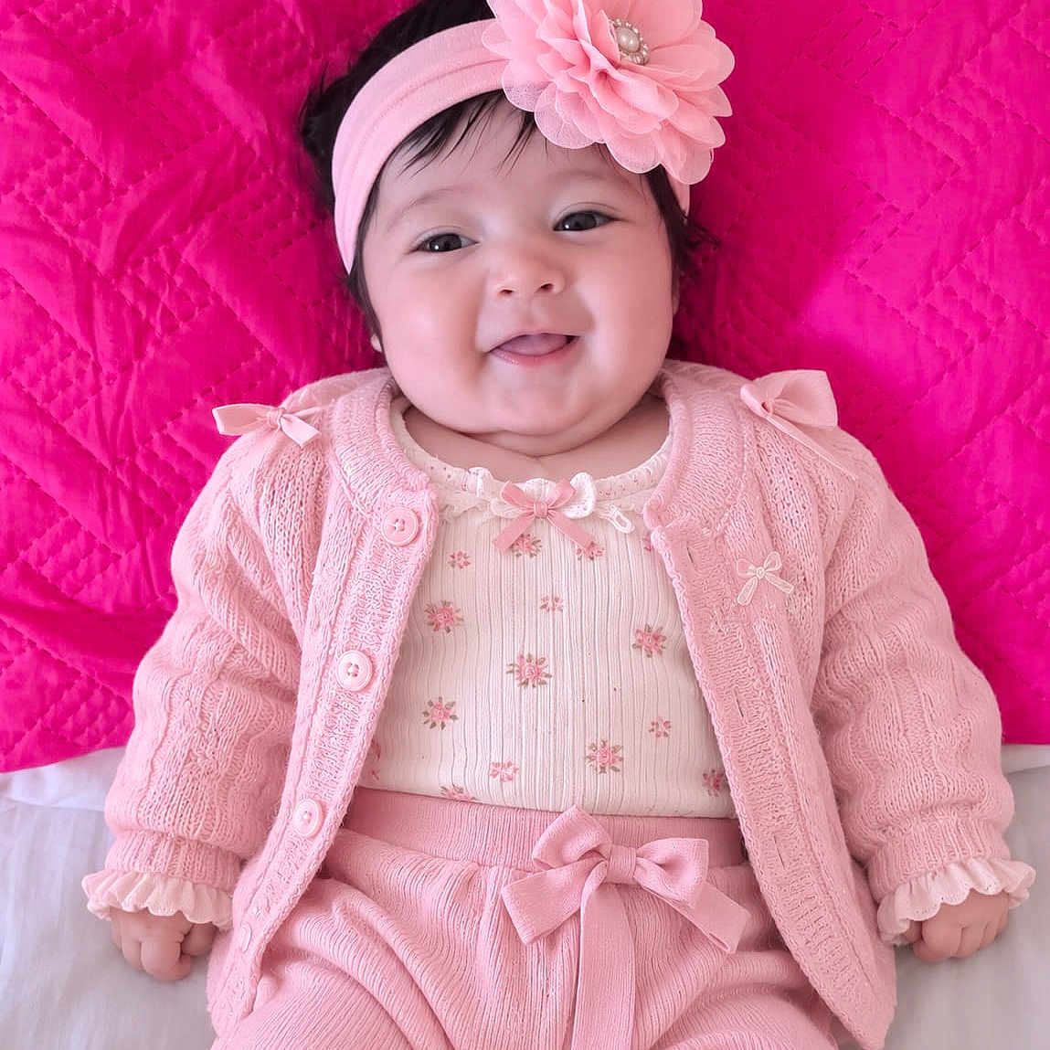 Maria is registered to the contest to win money with this photo: baby, infant, child, portrait, smiling, sitting, pink, headband, flower, clothing, sweater, dress, bow, quilt, blanket, indoors, close_up, cute, fashion, happy