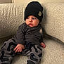 Cohen is registered to the contest to win money with this photo: baby, child, beanie, hat, couch, clothing, patterned_pants, socks, sitting, indoors, person, face, expression, looking_away, cozy, texture, casual, cute, smiley_patch, comfortable