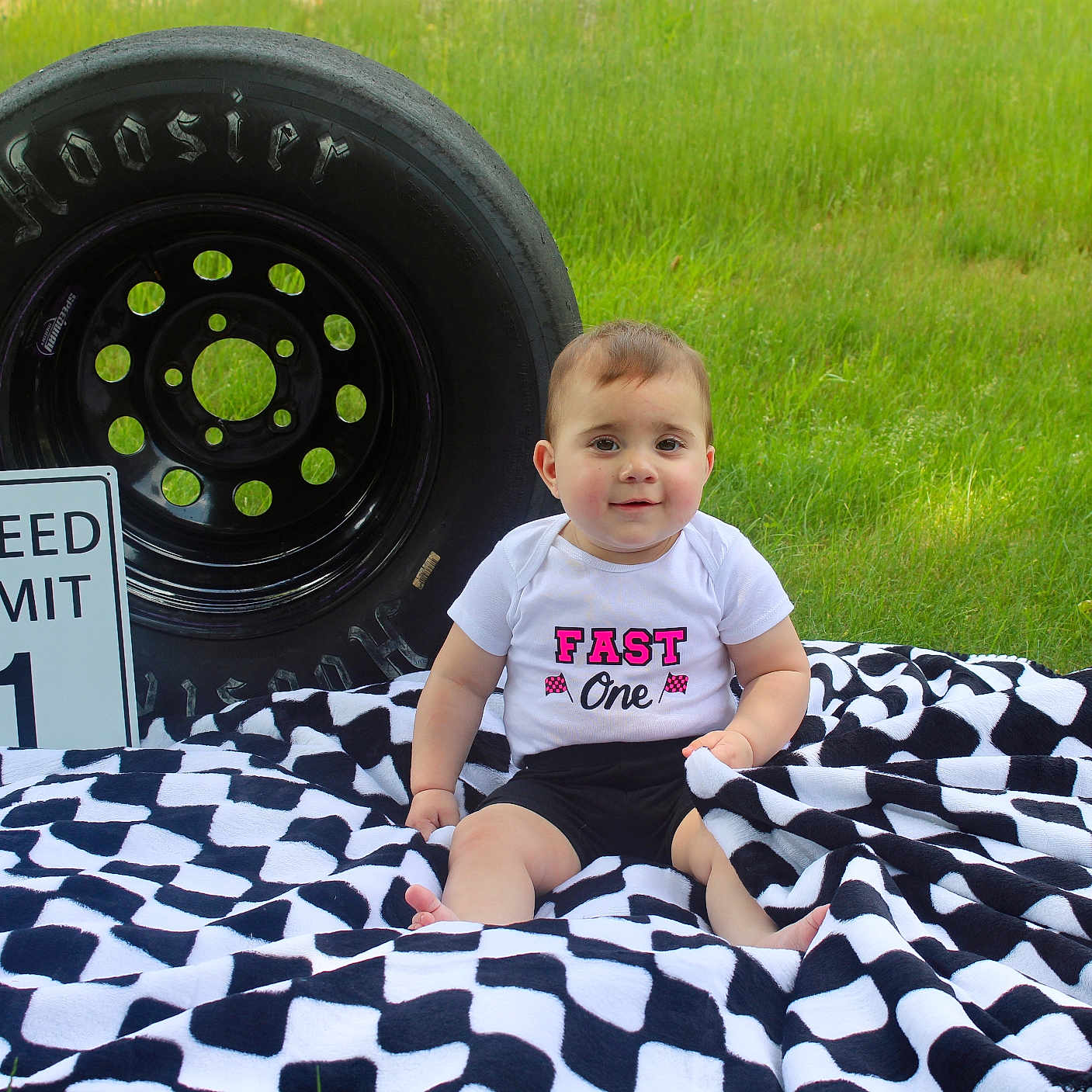 Mallory is registered to the contest to win money with this photo: alloywheel, baby, car, carwheel, clothing, face, grass, head, machine, person, photography, plant, portrait, sitting, spoke, t_shirt, tire, transportation, vehicle, wheel