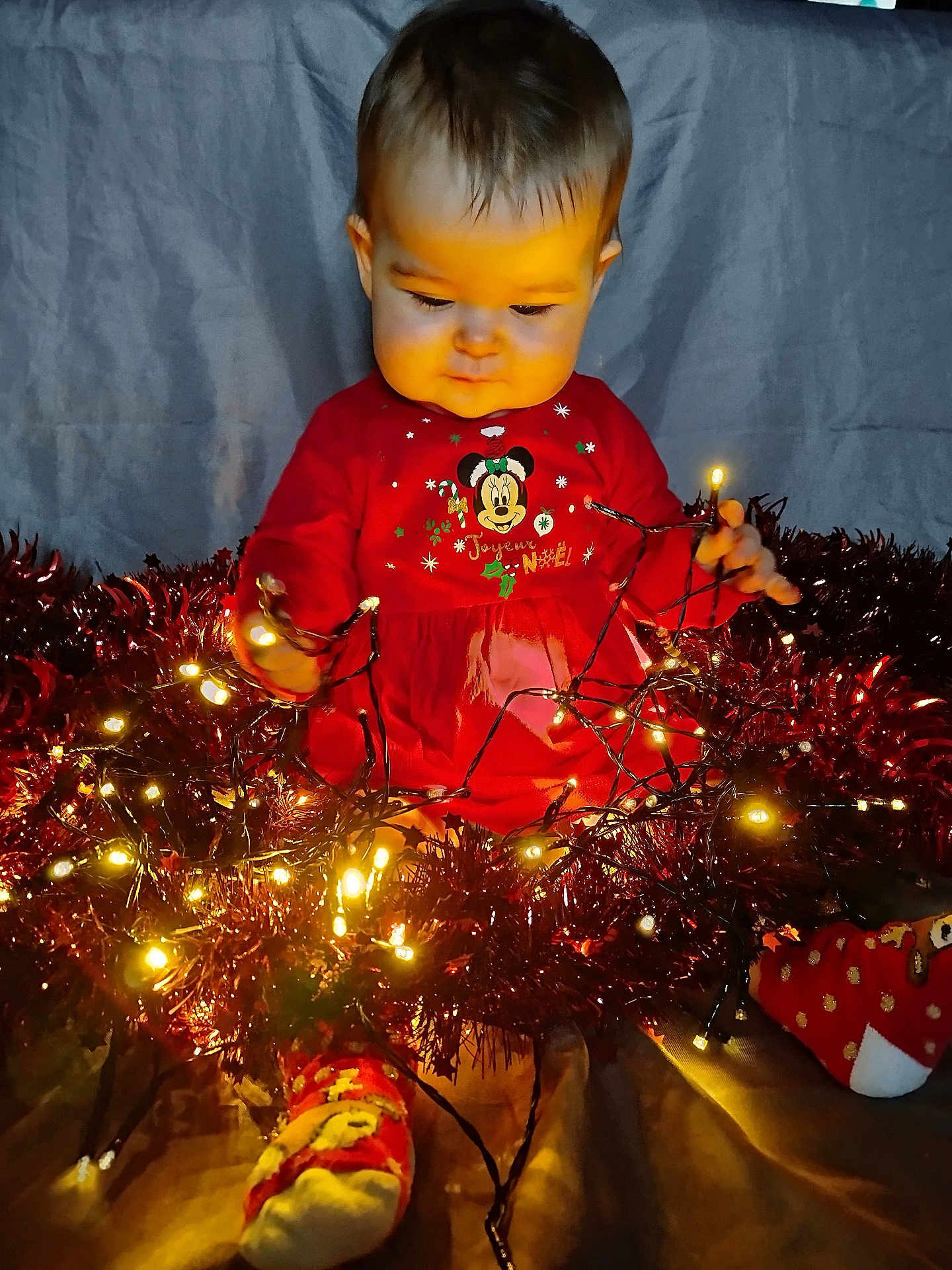 Gabie participe au concours pour gagner de l'argent avec cette photo : baby, child, christmas_lights, tinsel, red_clothing, socks, holiday, festive, indoors, glowing, string_lights, cute, toddler, celebration, smiling, decoration, warm_light, person, sitting, background