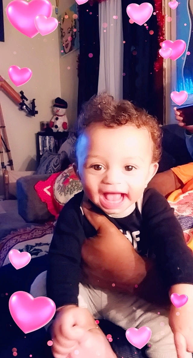 Giovani is registered to the contest to win money with this photo: baby, baby_toddler_clothing, cheek, child, finger, heart, interior_design, living_room, love, magenta, nail, party, party_supply, person, picture_frame, pink, room, stuffed_toy, thumb, toddler