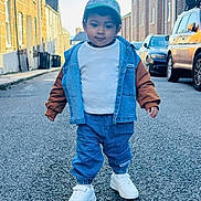 Apaar is registered to the contest to win money with this photo: asphalt, buildings, cap, casual_clothing, child, confidence, cool, daytime, denim_jacket, fashion, outdoor, person, sidewalk, small_person, street, toddler, urban, walking, white_shoes, young_child