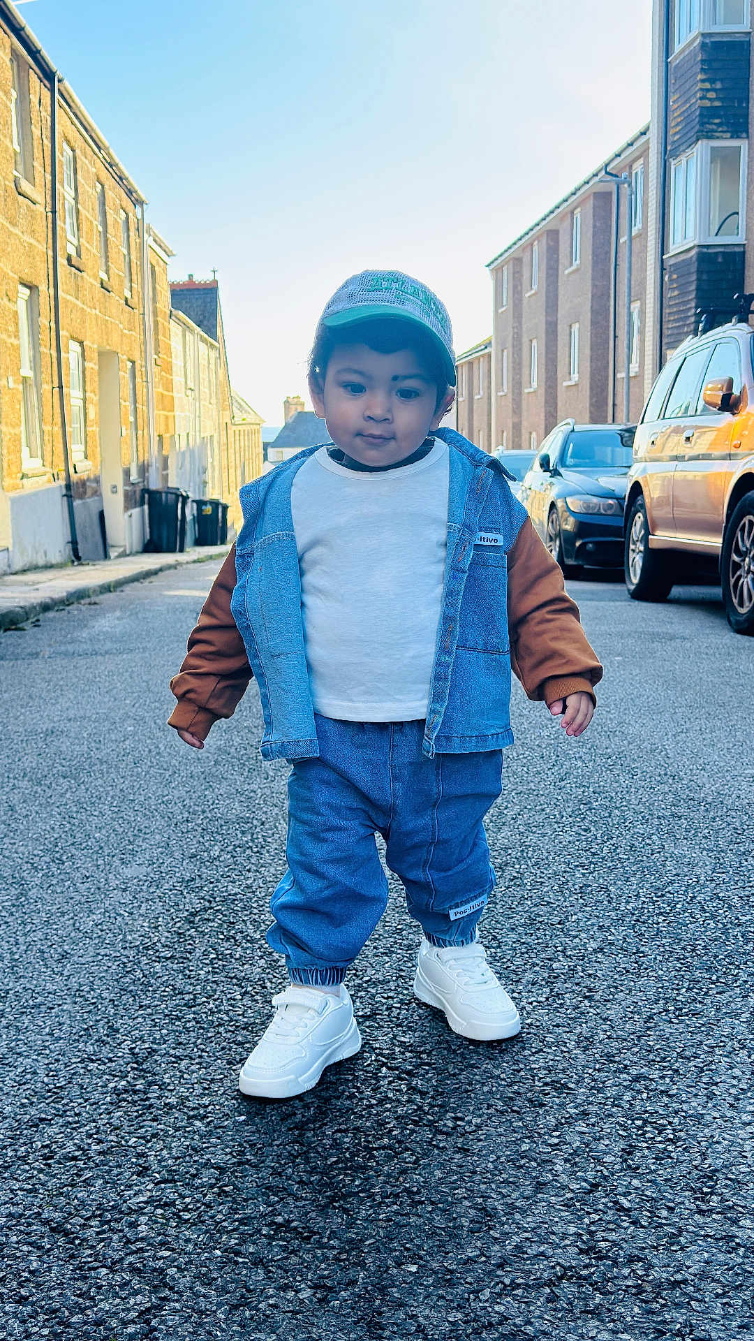 Apaar is registered to the contest to win money with this photo: asphalt, buildings, cap, casual_clothing, child, confidence, cool, daytime, denim_jacket, fashion, outdoor, person, sidewalk, small_person, street, toddler, urban, walking, white_shoes, young_child