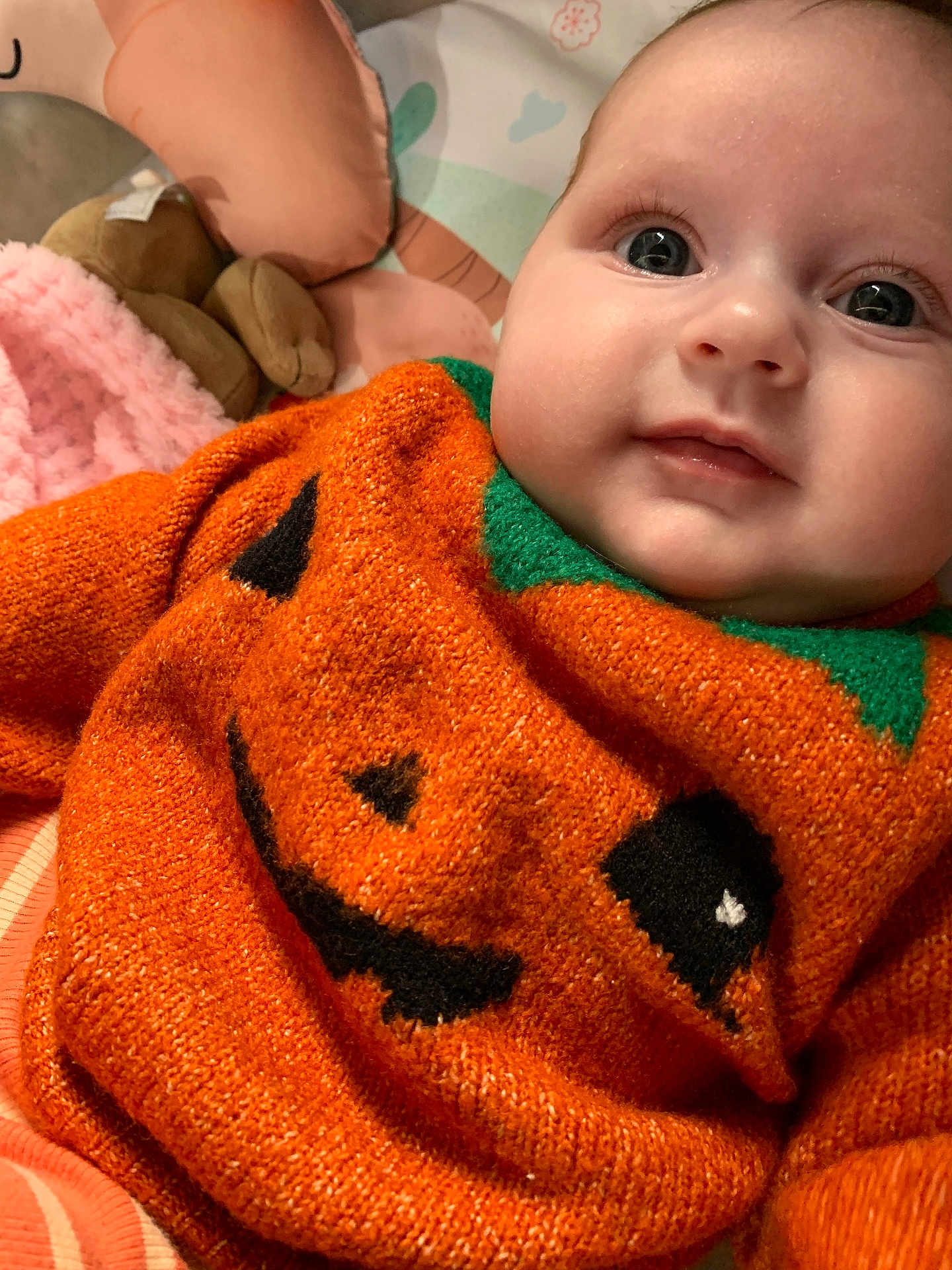 Esme is registered to the contest to win money with this photo: baby, infant, orange_sweater, jack_o_lantern, cute, close_up, plush_toy, blanket, soft_texture, portrait, child, face, eyes, smile, cozy, indoors, knitwear, holiday_theme, happy, clothing