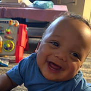 Khaisen is registered to the contest to win money with this photo: baby, smiling, blue_shirt, indoor, toys, carpet, face, child, happy, portrait, crawling, room, floor, furniture, infant, head, skin, cheerful, expression, home