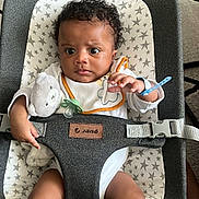 Isaac participe au concours pour gagner de l'argent avec cette photo : baby, baby_seat, bib, carpet, child, clothing, curly_hair, cute, expression, indoor, infant, pacifier, person, seatbelt, sitting, star_pattern, teddy_bear, toy, wooden_floor, young_child