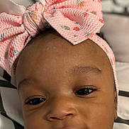 Brianna is registered to the contest to win money with this photo: baby, infant, headband, pink_bow, face, close_up, portrait, sleepwear, child, cute, smile, skin, eyes, nose, mouth, lying_down, blanket, phone_screen, lock_screen, time_display