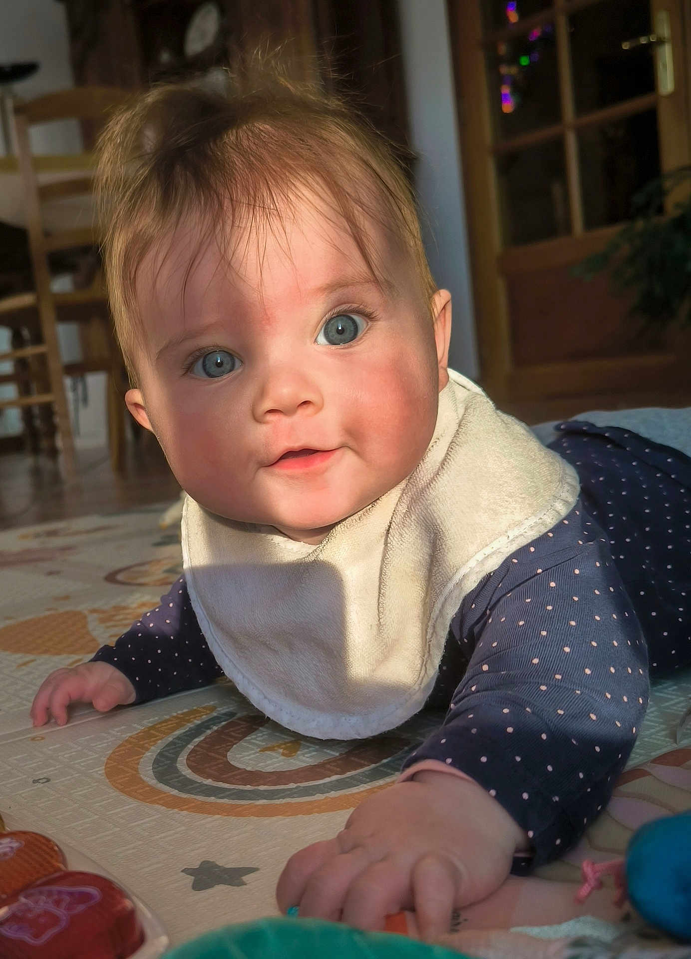 Alix a rejoint le concours — aidez-le/la à gagner de superbes lots ! baby, infant, bib, blue_eyes, wide_eyes, crawling, play_mat, polka_dots, long_sleeves, hand, face, indoor, sunlight, shadow, door, furniture, wooden_chair, toy, portrait, cute