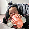 Malia is registered to the contest to win money with this photo: baby, child, high_chair, sippy_cup, drinking, infant, indoor, furniture, table, person, hands, face, clothing, calm, young_child, room, door, bottle, feeding, cute
