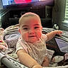 baby, infant, playpen, smile, reaching_hand, indoor, television, woman_on_tv, blanket, window, furniture, soft_toys, child, person, home, cushion, clothing, face, head, light