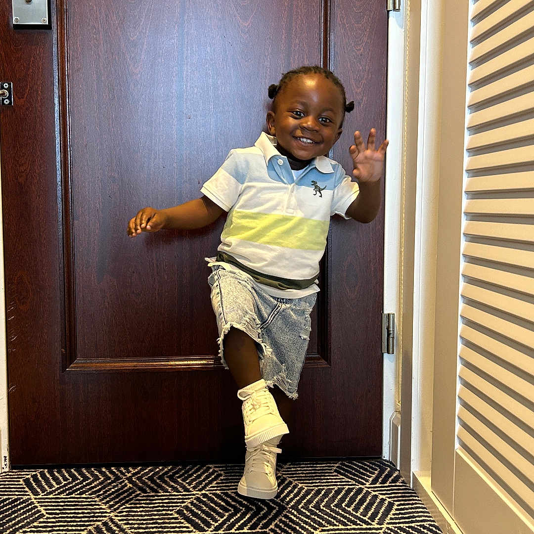 Keoon participe au concours pour gagner de l'argent avec cette photo : toddler, child, smiling, door, carpet, indoor, happy, waving, footwear, shorts, shirt, pattern, floor, hair, person, pose, wall, home, playful, young