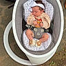 newborn, baby, sleeping, infant, rocker, baby_seat, headband, bow, clothing, onesie, booties, harness, car_seat, baby_gear, indoor, outdoor, carpet, ground, portrait, family