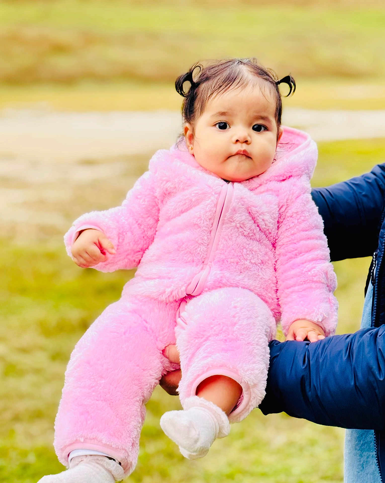 Elissa joined the competition — help win amazing prizes! baby, child, pink_clothing, outdoor, person, cute, fluffy, onesie, holding, hands, grass, portrait, young_child, face, sock, warm_clothing, expressionless, person_holding, winter_wear, small_child
