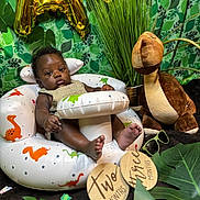 Asher joined the competition — help win amazing prizes! baby, infant, child, dinosaur, plush_toy, inflatable_chair, milestone_sign, greenery, leaves, plant, background, portrait, cute, indoor, sunglasses, decor, photography, smile, face, feet
