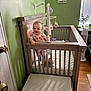 Luciana is registered to the contest to win money with this photo: baby, blanket, child, crib, door, floor, flower_sign, furniture, green_wall, happy, indoor, mobile, person, plant, room, smiling, sunlight, toy, window, wooden_crib
