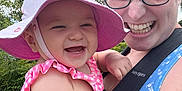 Luciana is registered to the contest to win money with this photo: adult, baby, baby_carrier, blue, child, closeup, cloudy_sky, glasses, greenery, happy, hat, laughing, nature, outdoor, person, pink, smiling, summer_clothing, sunhat, trees