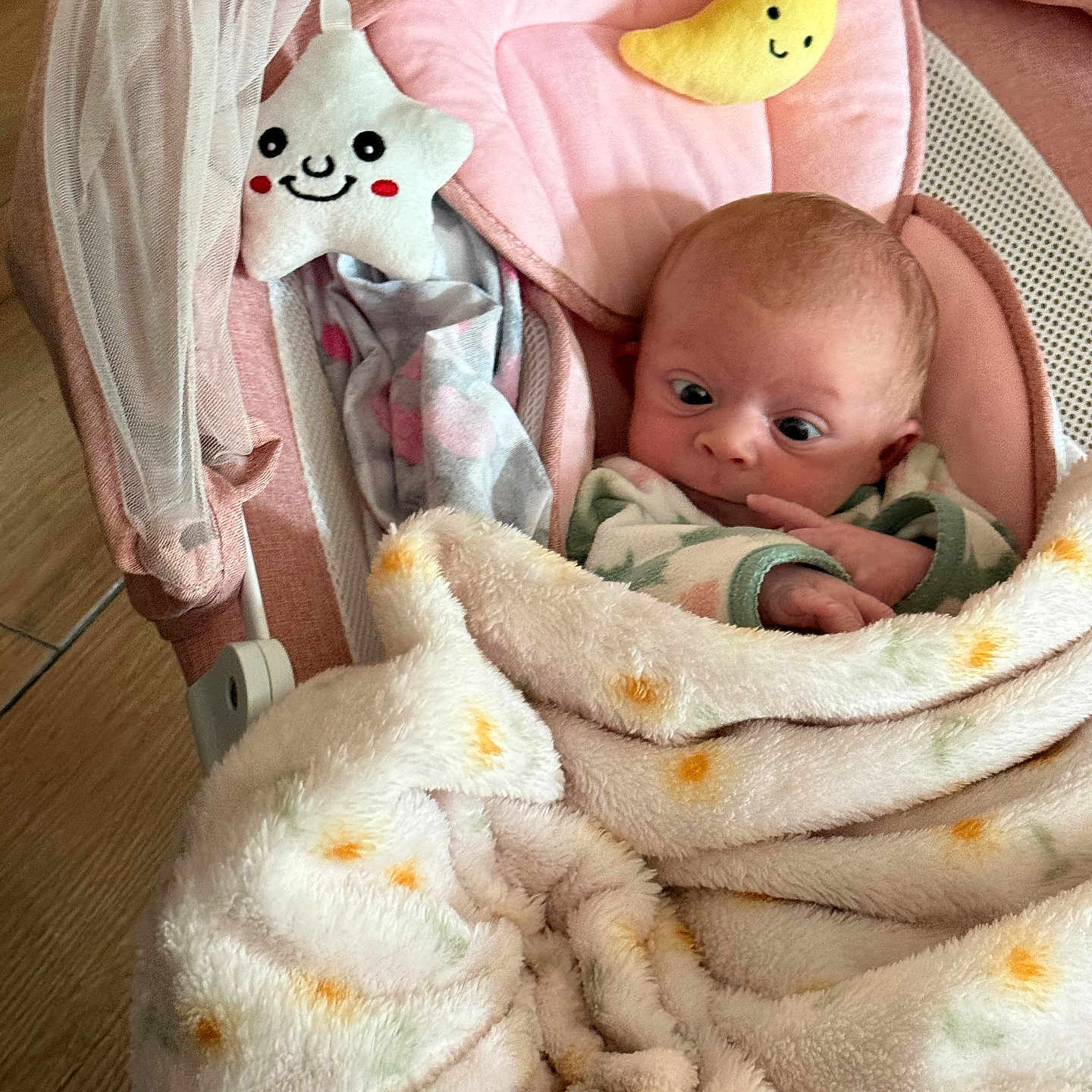 Bailey is registered to the contest to win money with this photo: baby, blanket, baby_seat, plush_toy, star_toy, moon_toy, floor, wooden_floor, face, wide_eyes, infant, pink, soft, cushion, sleepwear, cozy, indoor, child, cute, wrapped