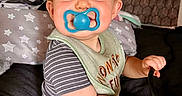 Caden is registered to the contest to win money with this photo: baby, child, infant, portrait, smiling, pacifier, striped_clothing, bib, sitting, bed, bedroom, pillow, blanket, indoor, face, eyes, hands, cozy, family_photo, playful