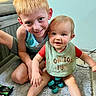 children, siblings, baby, boy, toddler, smiling, happy, portrait, indoor, home, carpet, couch, toy, playtime, blond_hair, blue_eyes, sitting, casual_clothing, bib, family
