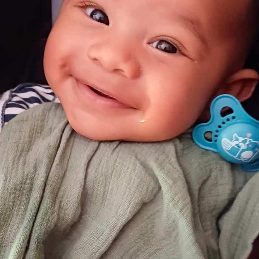 Uriel participe au concours pour gagner de l'argent avec cette photo : baby, blanket, cheeks, child, closeup, clothing, cute, expression, eyes, face, hand, happy, head, indoors, infant, pacifier, person, portrait, skin, smiling