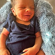 Zamarii is registered to the contest to win money with this photo: newborn, baby, smiling, infant, blue_blanket, onesie, sleeping, peaceful, cute, soft_texture, closeup, portrait, tiny_hands, skin, child, indoors, warm_light, cozy, resting, human